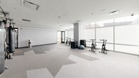 Located at 55 Clinton Pl in New Rochelle, NY, this single-floor fitness center offers a generously sized, well-appointed facility designed to support a full range of workout disciplines. The space is divided into distinct functional zones, each thoughtfully equipped and unified by a striking geometric-patterned carpet in neutral tones of gray, beige, and white.

The main cardio area lines an expansive wall of floor-to-ceiling windows, flooding the space with natural light and providing open views of the surrounding New Rochelle skyline. This zone houses a full row of FreeMotion treadmills and ellipticals, a StairMaster, rowing machines, and stationary bikes — all equipped with individual screens. Adjacent to this is a comprehensive strength training area featuring cable machines, multi-station weight racks, dumbbells, benches, and a mirrored wall that enhances the sense of spaciousness.

A dedicated studio space offers a more open layout, ideal for cycling classes, functional training, and group workouts. This area includes spin bikes, balance equipment, and heavy bags with accessory racks. A large wall-mounted display adds to the studio's versatility.

Throughout, recessed and flush-mounted ceiling lighting ensures consistent illumination, while direct access to an outdoor terrace with green space connects the interior to the fresh air of the surrounding urban environment.