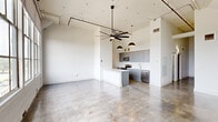 Located at 3700 Orleans Ave in New Orleans, this 2-bedroom, 1-bathroom unit showcases a contemporary industrial aesthetic throughout. The open-concept living and kitchen area immediately impresses with soaring ceilings, polished concrete floors, and an abundance of natural light streaming through large multi-pane windows. A striking oversized ceiling fan anchors the living space, while pendant lights with matte gold dome shades add warmth above the kitchen.

The kitchen is well-appointed with sleek gray cabinetry extending to the ceiling, stainless steel appliances including a range, microwave, refrigerator, and dishwasher, complemented by a spacious white quartz island and countertops with an undermount sink. A bright hallway connects the living area to the private quarters, where both bedrooms feature plush carpeting, elevated ceilings with ceiling fans, and clerestory windows that bring in natural light while maintaining privacy. Each bedroom is supported by a dedicated closet with built-in shelving and hanging rods.

The bathroom is finished in a clean, modern style with gray vanity cabinetry, a white quartz countertop, and a glass-enclosed walk-in shower with bold black hardware accents. The overall design of this unit blends industrial character with refined, contemporary finishes.