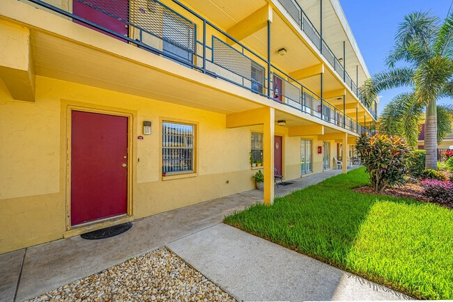 Encantador exterior de apartamento con paredes de color amarillo brillante, puertas rojas y un paisajismo vibrante con palmeras. - Parkview Apartments