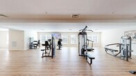 Located at 6039 Seminole Trail in Barboursville, Virginia, this fitness center offers a generously sized, single-floor workout facility designed to accommodate a wide range of exercise needs. The space is finished with warm-toned hardwood-style flooring throughout, contributing to a clean, welcoming atmosphere that encourages activity.

The main workout area is thoughtfully organized to maximize usability. A robust selection of strength training machines is distributed across the floor, including cable and multi-function weight machines, adjustable benches, and a well-stocked dumbbell rack with color-coded free weights. A dedicated stretching and functional training zone features stability balls, medicine balls, and a fold-out mat, providing ample room for dynamic warm-ups and cooldowns.

Cardio equipment, including stationary bikes and other aerobic machines, lines portions of the room, each positioned near the large windows that line the walls. These windows invite abundant natural light and provide outdoor views, creating an airy, open ambiance. Wall-mounted flat-screen televisions are strategically placed for entertainment during workouts.

The interior features neutral beige walls, recessed and flush-mount lighting, and a tray ceiling detail that adds subtle architectural definition. A mirrored wall expands the sense of space visually, while glass-panel entry doors provide a bright, accessible entryway. The overall design is functional, modern, and well-maintained.