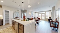 Located at 20130 Schiel Rd in Cypress, TX, this thoughtfully designed single-story residence offers a contemporary open-concept floor plan with clean lines and modern finishes throughout. The kitchen serves as the heart of the home, featuring a large central island with quartz countertops, pendant lighting, two-tone cabinetry, a subway tile backsplash, and a full suite of stainless steel appliances including a refrigerator, range, and built-in microwave. The island provides seating and flows seamlessly into a dedicated dining area and an expansive living room. The living room is filled with natural light from large windows and French doors that open to outdoor views, creating a bright and welcoming atmosphere. Light wood-style flooring runs throughout the main living areas, adding warmth and continuity. The primary bedroom is generously sized with large windows framing outdoor views, and is complemented by a well-appointed en-suite bathroom featuring a soaking tub and shower combination, quartz vanity, and tile flooring. A spacious walk-in closet with built-in shelving and hanging rods offers exceptional storage. Additional bedrooms are equally well-lit and comfortable. A dedicated in-unit laundry area with washer and dryer is conveniently accessible from the kitchen. The overall ambiance is modern, clean, and inviting.