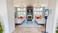 Located at 8201 Vaughn Rd in Montgomery, Alabama, this single-story community clubhouse offers a thoughtfully designed gathering space for residents. The main lounge is the centerpiece of the clubhouse, boasting soaring ceilings, herringbone-patterned wood-look flooring, and an abundance of natural light streaming through large, floor-to-ceiling windows that frame views of the outdoor pool and palm trees. A dramatic shiplap accent wall anchors a classic white fireplace, while two statement cage-style pendant chandeliers add a refined, contemporary touch. Tufted seating arrangements and vibrant accent décor create a warm and welcoming ambiance throughout. The kitchen area is outfitted with white cabinetry, granite-style countertops, and full appliances including a range, microwave, dishwasher, and refrigerator, making it well-suited for community events and gatherings. A dedicated fitness center rounds out the amenities, featuring cardio equipment including multiple treadmills and elliptical machines, a weight bench, a dumbbell rack, and floor-to-ceiling mirrors that expand the sense of space. The fitness room is brightened by natural light from multiple windows and accented with bold blue walls. Together, these spaces offer a complete and functional community hub.