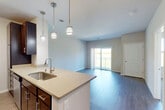 This thoughtfully designed single-floor residence offers a practical and modern layout across a comfortable footprint. The open-concept kitchen and living area form the heart of the home, characterized by rich dark-wood cabinetry, light quartz countertops, and stainless steel appliances. A peninsula with an undermount sink and stylish pendant lighting serves as a natural divider between the kitchen and the living space. The kitchen features a galley-style configuration with ample cabinet storage on both sides and updated hardware throughout. The living area is bathed in natural light from sliding glass doors that open onto a private balcony, offering pleasant outdoor views of lush greenery. Durable wood-style flooring flows throughout the main living areas, while plush carpet adds warmth to the bedroom. The bedroom is a comfortable retreat featuring a large window with outdoor views and direct access to a walk-in closet equipped with built-in shelving and hanging rods. The full bathroom includes a dark wood vanity with a single sink, a large mirror framed by bright vanity lighting, and a full tub-shower combination. Neutral tones and clean lines throughout the space create a cohesive, move-in-ready aesthetic.