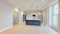 Located on Philadelphia's iconic South Broad Street, this 2-bedroom, 3-bathroom residence delivers a refined modern living experience across a single thoughtfully laid-out floor. Light wide-plank hardwood flooring flows continuously throughout, unifying the open-concept living and kitchen areas with a clean, cohesive aesthetic.

The kitchen is a standout feature, centered around a large dark-toned island with a sleek white quartz countertop and a brass-finish faucet. White shaker cabinetry, a subway tile backsplash, and stainless steel appliances — including a French door refrigerator and range — complete the space. Pendant lighting above the island adds warmth and style. Tall windows in the adjacent living area invite abundant natural light and offer views of the surrounding cityscape.

The generously sized primary bedroom features two large windows framed by ornate ironwork railings, providing urban character and natural light. Its en-suite bathroom is elegantly appointed with a wood-toned double vanity, white countertops, black fixtures, and a glass-enclosed shower featuring detailed mosaic tile flooring and textured subway tile walls. Walk-in closets with built-in shelving and hanging systems provide excellent storage throughout.

The additional bedroom is well-proportioned with its own closet access, complemented by bold dark-panel doors that contrast beautifully against the light floors and neutral walls. Three full bathrooms ensure convenience and comfort for all occupants.