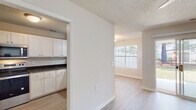 This single-story unit at 205 Partners Way in Fayetteville, NC offers a well-organized, functional layout with a clean, neutral aesthetic throughout. Light wood-style flooring flows consistently across the living areas and bedrooms, complemented by warm beige walls, white trim, and textured ceilings that contribute to a cohesive, move-in-ready appearance.

The kitchen is a standout feature, equipped with white shaker-style cabinetry, dark granite countertops, a stainless steel undermount sink with a matte black faucet, and a dishwasher. A window above the sink allows natural light to filter in, enhanced by a pendant light fixture overhead.

The living area is bright and open, featuring a ceiling fan and a sliding glass door that leads to an outdoor patio, offering views of mature trees and green space. A large front-facing window further contributes to the natural light throughout the space.

The bedrooms are comfortably sized, each featuring ceiling fans, light flooring, and closets with sliding or hinged doors. The primary bedroom includes direct access to an en-suite bathroom and an additional closet. Bathrooms are finished with white tile tub-shower combinations and granite-topped vanities, maintaining the unit's consistent design palette.