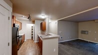 Located in Spokane, WA, this single-floor residence offers three bedrooms and two bathrooms within a well-organized, functional floor plan. The open-concept kitchen and living area serves as the heart of the home, where warm wood cabinetry, light countertops, and a peninsula with a double sink create a practical and inviting cooking space. Track lighting illuminates the kitchen, which is equipped with black appliances including a refrigerator, range, and microwave. A convenient walk-in pantry adds generous storage. Hardwood-style flooring runs through the kitchen, transitioning to plush carpet in the living room and bedrooms. The spacious living room features a sliding glass door that opens to a patio, filling the space with natural light and providing outdoor access. Each bedroom is carpeted and includes a closet with arched panel doors, offering ample storage. Secondary bedrooms feature large windows that bring in natural light. Both bathrooms are finished with wood-tone vanities and light countertops; one includes a baseboard heater, while the other features a full tub-shower combination. Neutral warm beige tones carry throughout the residence, creating a cohesive and comfortable ambiance.