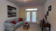 Located at 9525 US-78 Hwy in Ladson, South Carolina, this single-floor residential space offers a functional and comfortable layout designed for everyday living. The living area serves as the heart of the home, featuring plush wall-to-wall carpeting that adds warmth underfoot. A set of French doors with transom window above floods the room with natural light, while sheer curtains and blinds provide privacy and light control. The neutral, light-toned walls create a clean and open ambiance, complemented by decorative wall art that adds a touch of personality to the space. The room comfortably accommodates a sofa and coffee table arrangement, making it well-suited for relaxation and entertaining. Recessed ceiling vents suggest a central HVAC system for year-round comfort. The overall aesthetic is practical and inviting, with a straightforward design that emphasizes livability. The French doors hint at access to an outdoor area, connecting the interior to the natural surroundings outside. This space offers a solid foundation for comfortable residential living in the Ladson, SC area.