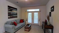 Located at 9525 US-78 Hwy in Ladson, South Carolina, this single-floor residential space offers a functional and comfortable layout designed for everyday living. The living area serves as the heart of the home, featuring plush wall-to-wall carpeting that adds warmth underfoot. A set of French doors with transom window above floods the room with natural light, while sheer curtains and blinds provide privacy and light control. The neutral, light-toned walls create a clean and open ambiance, complemented by decorative wall art that adds a touch of personality to the space. The room comfortably accommodates a sofa and coffee table arrangement, making it well-suited for relaxation and entertaining. Recessed ceiling vents suggest a central HVAC system for year-round comfort. The overall aesthetic is practical and inviting, with a straightforward design that emphasizes livability. The French doors hint at access to an outdoor area, connecting the interior to the natural surroundings outside. This space offers a solid foundation for comfortable residential living in the Ladson, SC area.