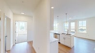 Located at 17-21 Park St in Essex Junction, Vermont, this well-appointed single-floor residence offers three bedrooms and two bathrooms across a thoughtfully designed layout. The open-concept kitchen and living area serves as the heart of the home, featuring white shaker-style cabinetry, marble-look countertops, a central island with a built-in sink, stainless steel appliances, and pendant lighting — all complemented by light hardwood-style flooring that extends throughout the main living spaces. Large windows in the living area flood the space with natural light while framing pleasant views of the surrounding Vermont landscape and greenery. The primary bedroom features hardwood-style flooring, a wall-mounted mini-split system, and expansive windows with outdoor views, while the additional bedrooms offer plush carpeting, natural light, and individual mini-split units for personalized climate control. One bedroom also includes direct access to a private balcony. The two bathrooms are finished with neutral tile flooring and tile surround — one featuring a soaking tub and the other a glass-enclosed walk-in shower — both with white vanities and modern fixtures. The overall aesthetic is clean, bright, and move-in ready.