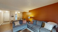 This single-floor residence offers a well-organized layout that balances comfort and functionality throughout its key living spaces. The living room serves as the heart of the home, distinguished by a striking burnt-orange accent wall that adds warmth and character to the space. Textured ceilings and a ceiling fan complement the room's cozy ambiance, while dark hardwood-style flooring grounds the space. A sliding glass door opens directly to a private outdoor patio, seamlessly connecting interior living with an exterior seating area — ideal for relaxing or dining al fresco. The galley-style kitchen features light wood cabinetry, granite-look countertops, tile flooring, and white appliances, with a window that allows natural light to filter in. The home includes two bedrooms, each with carpet flooring and closet storage. One bedroom features a window with outdoor views, while the other offers a clean, simple layout with a sliding closet door. The bathroom is fitted with a tub-shower combination in a bright, neutral finish. Throughout the home, textured ceilings and a consistent, neutral color palette create a cohesive and inviting atmosphere suited for everyday living.