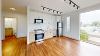 Located at 4240 Chestnut Street in Philadelphia's University City neighborhood, this two-bedroom, one-bathroom unit offers a clean, modern design across a single floor. Warm hardwood-style flooring runs throughout the entire space, creating a cohesive and inviting aesthetic.

The open kitchen is well-appointed with white cabinetry, stainless steel appliances including a gas range, microwave, dishwasher, and refrigerator, complemented by sleek track lighting overhead. The kitchen flows naturally into the living area, maximizing the functionality of the layout.

Both bedrooms are bright and well-proportioned, each featuring large windows that invite generous natural light and offer views of the surrounding Philadelphia cityscape and neighborhood rooftops. Each bedroom is equipped with a wall-unit HVAC system and includes a dedicated closet with built-in shelving and hanging rods for ample storage.

The hallway connecting the rooms also features a double-door closet, providing additional storage space. The bathroom is neatly finished with wood-tone cabinetry, a gray countertop vanity, a framed mirror with overhead lighting, and a shower-tub combination with white tile surround.

Clean white walls, modern fixtures, and an efficient floor plan make this a highly functional urban living space.