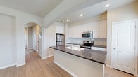 Located at 5811 102nd Street in Lubbock, Texas, this single-story home offers a thoughtfully designed layout with clean, modern finishes throughout. The kitchen serves as a centerpiece of the home, showcasing crisp white shaker-style cabinetry that extends to the upper walls, providing generous storage. Dark quartz countertops offer a striking contrast against the light cabinetry, and a large kitchen island with an integrated sink adds both functionality and workspace. Stainless steel appliances, including a refrigerator, range, and over-the-range microwave, complete the well-appointed kitchen. A subway tile backsplash adds a classic, polished touch. The space benefits from recessed lighting and vaulted ceiling lines that lend an open, airy feel to the interior. Light wood-look flooring runs throughout, contributing warmth and continuity between spaces. Charming arched doorways add architectural character and elegantly connect the kitchen to the adjoining hallway and living areas. Natural light filters in through the hallway, brightening the interior and enhancing the home's welcoming ambiance. The overall design balances modern aesthetics with practical, everyday livability.