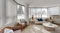 Located at 200 Denistoun St in Welland, Ontario, this well-appointed one-bedroom, one-bathroom unit offers a thoughtfully designed single-floor layout with a clean, neutral aesthetic throughout. The living and dining area is the highlight of the space, featuring a striking curved wall of floor-to-ceiling wraparound windows fitted with vertical blinds that bathe the room in abundant natural light and offer open views of the surrounding landscape. The living area is finished with soft carpeting and connects seamlessly to the dining space, creating a comfortable, open-concept feel. The kitchen is efficiently designed with crisp white cabinetry, stone-look countertops, a double stainless steel sink, and a stainless steel electric range, offering a fresh and functional cooking environment with light tile flooring. The carpeted bedroom is a calm, well-lit retreat with a large window, a built-in sliding-door closet, and ample room for a sleeping and workspace arrangement. A carpeted hallway with sliding storage doors and wall art connects the main living spaces to the private areas. The bathroom features a full-size soaker tub and shower combination with clean white surroundings and chrome fixtures, completing this comfortable and move-in-ready home.