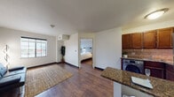This single-floor unit offers a thoughtfully designed layout that connects the living, dining, and kitchen areas in an open, cohesive arrangement. Rich hardwood-style flooring runs throughout the main living spaces and bedroom, lending warmth and visual continuity to the interior.

The living area is well-proportioned, featuring neutral walls, dark baseboards, and a large window that introduces natural light and outward views of the surrounding neighborhood. The kitchen is efficiently designed with warm-toned wood cabinetry extending to the upper walls, a tile backsplash, dark granite countertops, and stainless steel appliances including a refrigerator and microwave. A peninsula counter with seating provides a convenient dining area. Notably, an in-unit washer is integrated within the kitchen space.

The bedroom is a calm, well-lit retreat featuring the same hardwood-style flooring, a stylish upholstered headboard with built-in sconce lighting, and a dresser with television.

The bathroom features light ceramic tile flooring, a wood vanity with granite countertop, and a full tub-shower combination with tile surround. A separate closet is accessible from the bathroom corridor, adding practical storage to the unit.