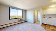 Located at 330 Oak Grove St in Minneapolis, Minnesota, this two-bedroom, one-bathroom unit offers a practical and well-organized layout across a single floor. The living area is bright and open, featuring plush wall-to-wall carpeting and a large picture window that frames elevated views of the Minneapolis cityscape and surrounding tree canopy, flooding the space with natural light. A wall-mounted HVAC unit and baseboard heating system provide year-round climate control. Adjacent to the living area, the compact kitchen is equipped with white cabinetry, a gas range, and tile flooring, offering an efficient workspace. A hallway connects the main living space to the rest of the unit, with a built-in shelving closet visible along the way. The spacious primary bedroom features soft carpeting and generous wall space, while the second bedroom includes a sliding-door closet for added storage. The bathroom is appointed with a full tub-and-shower combination, fully tiled in classic white subway tile with chrome fixtures. Throughout the unit, neutral tones and clean lines create a straightforward, functional living environment well-suited for urban Minneapolis living.