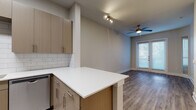 This single-floor residence showcases a contemporary design with a cohesive, neutral color palette throughout. The open-concept kitchen flows directly into the living area, creating a functional and connected layout. The kitchen is outfitted with flat-front cabinetry in a warm taupe finish, white quartz countertops, a classic white subway tile backsplash, and a full suite of stainless steel appliances, including a refrigerator, electric range, over-the-range microwave, and dishwasher. A peninsula with additional cabinetry extends the counter space and provides a natural transition into the living area.

The living space is bright and open, benefiting from natural light that enters through a set of French doors leading to an outdoor area. A ceiling fan with a light fixture keeps the space comfortable. Wood-look plank flooring runs continuously through the living areas, adding warmth and visual consistency.

The bedroom is generously sized with a clean, neutral finish and access to what appears to be a closet area. The bathroom features large-format tile flooring, a tub-shower combination with white subway tile surround, a toilet, and a vanity with matching taupe cabinetry. The overall design is clean, functional, and move-in ready.