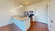 This single-floor residence at 147 N Harold St in Salt Lake City, UT, offers a well-organized layout with a clean, modern aesthetic throughout. The kitchen serves as a central feature, boasting white cabinetry, light granite-style countertops, and stainless steel appliances including a refrigerator, range, and microwave. A peninsula with a double-basin sink and pendant lighting above separates the kitchen from the living and dining area, which benefits from large windows that admit generous natural light and views of the surrounding greenery.

Hardwood-style flooring flows through the main living areas, lending warmth and visual continuity. The bedrooms are finished with plush carpeting for added comfort, and one bedroom includes access to a spacious walk-in closet outfitted with built-in shelving and double hanging rods, providing ample storage. An additional carpeted room offers flexible use as a bedroom or secondary space.

A dedicated laundry nook houses a stacked washer and dryer unit, adding convenience within the home. The bathroom features a white vanity with a granite-style countertop, a large mirror, tile flooring, and a full tub-shower combination. Overall, the unit presents a bright, neutral palette and practical finishes throughout.