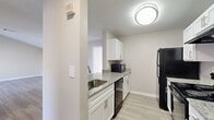 This single-floor residence offers four bedrooms and three bathrooms within a thoughtfully organized layout. The galley-style kitchen is a standout feature, showcasing white shaker cabinetry, granite-look countertops, a stainless steel sink, and black appliances including a range, dishwasher, microwave, and refrigerator. Light wood-look flooring runs through the kitchen, adding a clean, modern aesthetic. The open living room is bright and airy, featuring light hardwood-style flooring and a neutral color palette that creates a welcoming atmosphere. The bedrooms are carpeted and well-proportioned, each equipped with ceiling fans and ample natural light. The primary bedroom offers a comfortable retreat with generous floor space. All three bathrooms maintain a consistent design with white vanities, tub-shower combinations, and light wood-look flooring, with some featuring windows for natural ventilation. A dedicated laundry area houses a full-size washer and dryer set with overhead wire shelving for additional storage. Throughout the home, neutral tones, clean finishes, and a practical floor plan come together to create a functional and comfortable living environment.