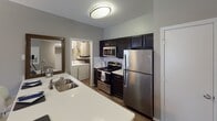 Located at 12235 Stone Arbor Way in Charlotte, NC, this single-floor residence offers a well-designed layout with thoughtfully appointed spaces throughout. The kitchen is equipped with stainless steel appliances, including a refrigerator, range, and built-in microwave, complemented by dark cabinetry, white countertops, and a double-basin sink. A convenient in-unit laundry area is accessible directly from the kitchen. The living room features wood-style flooring, neutral gray walls, a textured ceiling, and a bright window with access to natural light, creating a welcoming gathering space. Multiple bedrooms are carpeted and share a soft, neutral color palette, each with windows dressed in layered blinds and curtains that allow for ample natural light. The primary bedroom offers a serene retreat with views of surrounding greenery. The bathrooms are finished with dark vanity cabinetry, white countertops, wood-style flooring, and framed mirrors with vanity lighting. One bathroom includes a soaking tub with a curtained surround, while another features a spacious vanity area with additional storage. Throughout the residence, a consistent modern aesthetic is maintained with neutral tones, tasteful finishes, and functional design.
