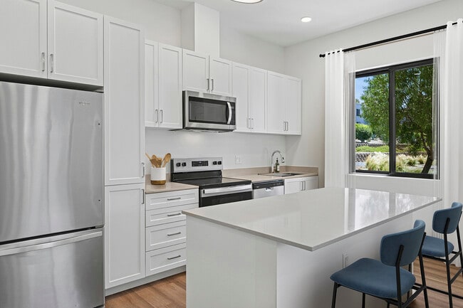 Coming Soon: Freestanding Home kitchen with stainless steel appliances, white cabinetry, beige quartz countertops, and hard-surface flooring - eaves San Marcos