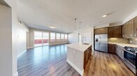 Located at 9830 W Tropicana Ave in Las Vegas, this well-appointed 3-bedroom, 3-bathroom residence offers a thoughtfully designed single-floor layout that balances comfort and functionality. The heart of the home is a generous open-concept living, dining, and kitchen area featuring wood-style flooring, recessed lighting, and pendant lights above a central island with a white quartz countertop and undermount sink. The kitchen is fully equipped with stainless steel appliances, rich dark-toned cabinetry, a tile backsplash, and a gas range, complemented by a dedicated pantry for additional storage. Sliding glass doors in the living area flood the space with natural light and lead to a private patio with open sky views. The spacious primary bedroom features plush carpeting and access to a well-sized walk-in closet with wire shelving throughout. The bathrooms are finished with dark wood vanities, quartz countertops, and glass-enclosed walk-in showers with tile accents. Additional bedrooms offer wood-style flooring and bright windows. The residence also includes a versatile den, a dedicated laundry room, five closets, and a hallway connecting all spaces seamlessly for a cohesive and practical living experience.