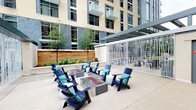 This contemporary multi-story building showcases thoughtful design both inside and out. The interior hallways are finished in a modern palette of deep charcoal and crisp white, accented with bold teal trim elements that add a striking visual identity. Patterned carpet in gray, teal, and white runs the length of the corridors, complementing the recessed lighting and linear ceiling accents that guide residents through the space. Each unit entrance is marked with a numbered placard and decorative tile art, adding a personalized touch to individual doorways fitted with keypad-accessible hardware.

The outdoor terrace is a standout communal feature, offering a spacious patio surrounded by warm cedar privacy fencing and lush greenery. At its center sits a sleek rectangular fire pit table, encircled by navy Adirondack chairs with teal cushions, creating an inviting gathering spot. A pergola-covered area with additional seating extends the outdoor living space, while views of the building's upper floors and balconies frame the terrace. The combination of modern finishes, cohesive color accents, and well-designed shared amenities gives the building a polished, resort-inspired atmosphere.