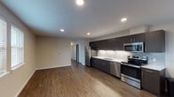 Located at 2220 SE 192nd Ave in Vancouver, Washington, this single-floor unit offers a thoughtfully designed, open-concept layout that seamlessly connects the living and kitchen areas. Rich hardwood-style flooring extends throughout the main living space, lending warmth and continuity to the interior.

The kitchen is a standout feature, outfitted with sleek dark espresso cabinetry that reaches to the ceiling, providing ample storage. Light countertops create a striking contrast, while a white subway tile backsplash adds a clean, modern touch. Under-cabinet lighting illuminates the workspace, and a full suite of stainless steel appliances — including a refrigerator, electric range, microwave, and dishwasher — completes the space.

The open living area benefits from multiple windows fitted with blinds, allowing natural light to filter in. A wall-mounted HVAC unit ensures year-round comfort. The bathroom is well-appointed with light tile flooring, a full soaking tub with shower, accessibility grab bars, a vanity with light countertops, and a window that brings in natural light. A stacked in-unit washer and dryer is also visible, adding everyday convenience. The overall aesthetic is clean, contemporary, and move-in ready.