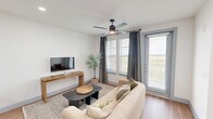 Located at 12820 Langston Blvd in Baytown, TX, this single-story 1-bedroom, 1-bathroom residence offers a well-designed layout that maximizes comfort and functionality. The open-concept living room and kitchen form the heart of the home, with the living area featuring wood-look flooring, a ceiling fan with light, and large windows dressed with gray drape panels and horizontal blinds that invite abundant natural light. The kitchen is a standout, showcasing warm wood-tone cabinetry extending to the ceiling, a large quartz waterfall island with an undermount sink and bar seating, stainless steel appliances, a white tile backsplash, and pendant lighting overhead. The spacious bedroom is carpeted for comfort, features natural light through sizable windows with blinds and curtains, a ceiling fan, and direct access to the dedicated closet and bathroom. The bathroom is finished with a wood-tone vanity, white quartz countertops, a wide mirror with bright overhead lighting, and large-format light tile flooring alongside a walk-in tiled shower. Gray-blue interior doors add a cohesive design detail throughout the home, creating a modern yet warm aesthetic.