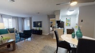 This single-floor residence offers a thoughtfully designed open-concept layout that seamlessly connects the living, dining, and kitchen areas. Wood-style flooring flows throughout the main living spaces, creating a cohesive and clean aesthetic, while a textured ceiling adds subtle architectural character overhead. The living room is generously proportioned, accommodating a full seating arrangement and wall-mounted television, with vertical blinds and grommet-style curtains framing the windows and allowing ample natural light. A ceiling fan enhances comfort in the adjoining dining area, which comfortably fits a round dining table and chairs.

The galley-style kitchen is efficiently designed with white cabinetry, granite-look countertops, a mosaic tile backsplash, and stainless steel appliances including a refrigerator, microwave, and dishwasher. The bedroom features plush carpeting, a wide mirrored sliding-door closet with built-in shelving, and a window with exterior views. Two full bathrooms are present, each finished with granite-topped vanities, wood-style flooring, and a shower-tub combination. A dedicated laundry area houses a full-size top-load washer and dryer, adding significant functional convenience to the residence.