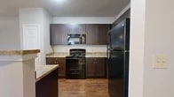 Located in Arlington, Texas, this single-story, two-bedroom, two-bathroom home offers a practical and comfortable layout across a well-proportioned floor plan. The combined kitchen and living room serves as the heart of the home. The kitchen is outfitted with dark espresso cabinetry, light stone-style countertops, a double-basin sink, and a full suite of black appliances including a refrigerator, electric range, and built-in microwave. A peninsula with pendant lighting adds both prep space and a natural divide from the living area. The living room features plush carpet, a ceiling fan with light kit, and large windows alongside a glass door that allow natural light to fill the space and provide outdoor views. The spacious primary bedroom includes dual windows, a ceiling fan, and connects to a walk-in closet with wire shelving systems. The second bedroom is carpeted and similarly well-lit. Three closets throughout the home provide ample storage, including a walk-in closet with hardwood-style flooring and built-in wire shelving. A central hallway connects all areas of the home efficiently. Neutral tones, white trim, and consistent finishes throughout lend the space a clean, cohesive aesthetic.