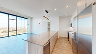 Located in Chicago's vibrant River West neighborhood, this contemporary 3-bedroom, 3-bathroom residence offers a refined urban living experience defined by clean lines and high-end finishes throughout. The open-concept living and dining area is anchored by dramatic floor-to-ceiling windows that flood the space with natural light and frame sweeping panoramic views of the Chicago skyline and surrounding cityscape. Exposed concrete ceiling details in the living area add an industrial edge that complements the modern aesthetic.

The kitchen is a standout, featuring a generous waterfall-edge island with seating, two-tone cabinetry combining white uppers with warm wood-toned lowers, a white tile backsplash, and a full suite of stainless steel appliances including a range, microwave, dishwasher, and refrigerator. Light wood-tone flooring runs seamlessly throughout the living spaces, enhancing the bright and airy atmosphere.

Each bedroom is well-proportioned, with the spacious primary suite offering abundant room and access to a dedicated closet. The bathrooms are elegantly finished with large-format tile flooring, dark wood vanities with backlit mirrors, undermount sinks, and a glass-enclosed walk-in shower in the primary bath. The thoughtful layout and quality craftsmanship make this residence a compelling offering in one of Chicago's most dynamic neighborhoods.
