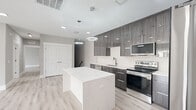 This well-appointed 3-bedroom, 2-bathroom home offers a thoughtfully designed single-floor layout with modern finishes throughout. The open-concept kitchen serves as the heart of the home, showcasing a striking marble-veined waterfall island, dark wood-grain cabinetry with sleek hardware, white subway tile backsplash, and stainless steel appliances. Dual circular pendant lights add a contemporary touch overhead, while light wood-look flooring flows seamlessly throughout the space. The living room is bright and airy, featuring recessed lighting and a sliding glass door that opens to a private balcony, filling the room with natural light and outdoor views. The generously sized primary bedroom includes a ceiling fan, a large window for natural light, and ample space for comfortable living. Two additional bedrooms offer versatile use, each finished with the same light flooring and clean white trim. Both bathrooms are elegantly finished with marble-look tile flooring, white quartz countertops, modern vanities with chrome fixtures, and backlit mirrors that enhance the clean, contemporary aesthetic. The consistent use of neutral tones, quality materials, and modern design elements creates a cohesive and inviting atmosphere throughout the entire home.