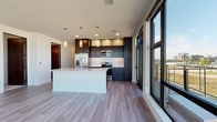 Located at 2140 Holmgren Way in Ashwaubenon, Wisconsin, this single-floor unit showcases a contemporary design with high-end finishes throughout. The open-concept kitchen and living area serves as the heart of the space, featuring a large central island with a white quartz countertop, undermount sink, and pendant lighting. Dark espresso cabinetry lines the kitchen walls, complemented by a white subway tile backsplash and stainless steel appliances, including a refrigerator, range, and microwave. Wide-plank flooring flows throughout the main living areas, enhancing the clean, modern aesthetic.

Floor-to-ceiling windows and glass doors frame sweeping outdoor views, flooding the space with abundant natural light. A dedicated living area boasts corner windows on two walls, creating a bright and panoramic atmosphere.

The bedrooms offer plush carpeting and large windows with roller shades for privacy. A spacious walk-in closet with multi-tier wire shelving provides generous storage. Two bathrooms feature dark vanity cabinetry, white quartz countertops, and large mirrors. The primary bathroom includes a walk-in shower, while the secondary bathroom provides additional convenience. The unit also includes access to an outdoor area through a glass door off the kitchen.