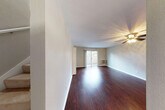 This two-floor residence offers a thoughtfully designed layout that balances comfort and functionality across both levels. The main floor features a spacious, open living area finished with rich, dark hardwood-style flooring that extends throughout. A ceiling fan anchors the living space, while a sliding glass door floods the room with natural light and provides direct access to an outdoor balcony area. Adjacent to the living space is a well-equipped kitchen showcasing warm wood cabinetry, dark granite-style countertops, a mosaic tile backsplash, and a full suite of stainless steel appliances including a refrigerator, dishwasher, and range. A window above the sink brings in additional natural light. The main floor also includes a bathroom with a window for ventilation. A carpeted staircase with a clean white handrail connects to the upper level, where the bedrooms are located. Each bedroom is finished with plush carpet and features mirrored sliding closet doors that enhance the sense of space and light. Windows in the upper-level rooms offer views of the surrounding greenery. Textured walls and crisp white baseboards are consistent throughout, lending the space a clean and cohesive aesthetic.