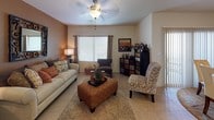 This single-floor residence offers a thoughtfully designed layout that balances comfort and functionality throughout. The inviting living room serves as the heart of the home, featuring tile flooring, a ceiling fan, and a striking warm-toned accent wall that anchors the space. Large windows fitted with blinds and curtain panels allow natural light to fill the room, while a front entry door with a transom window provides a welcoming arrival point.

The kitchen is equipped with light wood cabinetry, tile flooring, and black appliances including a refrigerator, electric range, and built-in microwave. A central island with a countertop workspace adds practical utility. Conveniently adjacent to the kitchen is an in-unit laundry area housing a full-size washer and dryer.

The primary bedroom is generously proportioned, featuring soft carpet, a tray ceiling with a pendant light fixture, and a large window that frames outdoor greenery. The room connects to additional spaces including a walk-in or closet area and an en-suite bathroom. The bathroom is finished with neutral stone-look tile throughout, a soaking tub with a tiled surround, and warm wood vanity cabinetry. A secondary bedroom mirrors the primary's comfort with plush carpeting and natural light. The overall ambiance is warm, cohesive, and move-in ready.
