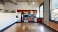 Located at 301-321 S 1st St in the heart of downtown San Jose, this single-floor unit blends industrial loft aesthetics with modern finishes to create a distinctive urban living space. The open layout makes efficient use of its footprint, with high ceilings featuring exposed wooden and concrete beams that add architectural depth and a raw, loft-like character throughout.

The kitchen is a standout feature, equipped with rich walnut-toned cabinetry, dark granite countertops, stainless steel appliances including a refrigerator, range, microwave, and dishwasher, and a slate tile backsplash. Polished concrete floors reflect natural light, while large black-framed windows with exposed brick surrounds offer direct views of the surrounding downtown streetscape.

The hallway connects the spaces with a sleek, functional design, highlighted by warm wall sconces, a built-in wood cabinetry entry unit, and a flush-mounted electrical panel. Polished concrete floors continue here, and a window at the end draws in natural light.

The bathroom is finished to a contemporary standard, featuring large-format neutral wall tiles, a vessel-style rectangular sink on a dark open vanity, a backlit round mirror, and a wall-mounted wood accent cabinet, lending the space a clean, modern sensibility.

An additional open room with carpeted floors and exposed ceiling beams provides flexible use as a living or sleeping area.