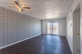 Located at 5267 Carousel Dr in El Paso, TX, this single-floor unit offers a functional and distinctive layout with consistent design elements throughout. The main living area makes a strong visual impression with a bold, large-format tiled accent wall in a cool gray tone, dark hardwood-style flooring, a ceiling fan, and a textured popcorn ceiling. Sliding glass doors lead to an outdoor balcony, allowing natural light to fill the space. An adjacent room provides additional flexible living space, also featuring hardwood-style flooring, vertical blinds, and access to natural light. The galley-style kitchen is efficiently designed with white cabinetry, marble-look countertops, a tiled backsplash, white appliances including a range and refrigerator, and a window that brings in natural light. The bedrooms continue the distinctive tiled accent wall design and are finished with plush carpet flooring and ceiling fans, creating a comfortable and cohesive feel. The bathroom features a full tub-shower combination with large-format marble-look tile surround, complemented by hardwood-style flooring. Overall, the space presents a clean, consistent aesthetic with practical finishes throughout.