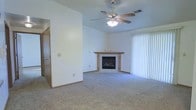 This single-floor residence at 2438 offers a comfortable and functional layout designed for everyday living. The living area serves as the heart of the home, featuring plush wall-to-wall carpeting that adds warmth underfoot. A corner fireplace with a wood-trimmed surround provides a focal point and a cozy atmosphere, making it an inviting space for relaxation. A ceiling fan with an integrated light fixture is centrally positioned overhead, ensuring year-round comfort and efficient air circulation. Large vertical blinds frame a sliding glass door that fills the room with natural light and provides direct access to the outdoors. Neutral white walls throughout create a clean, versatile backdrop that accommodates a variety of décor styles. A doorway visible from the living space leads further into the home, hinting at additional rooms beyond. The overall ambiance is bright, open, and move-in ready, with understated finishes that offer a welcoming, practical living environment suitable for a range of lifestyles.