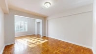This single-floor unit offers a well-organized and functional layout that makes efficient use of its space. The living area is immediately inviting, characterized by classic parquet wood flooring in a rich warm tone that adds texture and visual warmth throughout. Natural light filters in through the windows, casting a bright, airy quality across the open rooms. The neutral, light-toned walls provide a clean and versatile backdrop throughout the unit.

The main living space is generously proportioned, featuring a built-in closet that offers practical storage. A flush-mount ceiling light fixture provides consistent illumination. The layout connects seamlessly to additional areas of the unit, allowing for an open, cohesive flow.

The kitchen is compact and practical, equipped with a gas range and oven, light-toned laminate countertops, and warm wood cabinetry overhead. The space is designed for efficient meal preparation.

The bathroom is finished in a crisp, all-white palette, featuring a combination bathtub and shower, a white vanity with under-sink storage, a toilet, and classic small-tile mosaic flooring. A frosted window allows natural light into the space while maintaining privacy.

Overall, this unit presents a clean, straightforward living environment with timeless flooring, functional built-ins, and a bright, neutral aesthetic throughout.