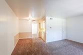This single-floor unit offers a practical and straightforward layout designed for comfortable everyday living. The living area greets residents at the front entry, featuring wall-to-wall carpet, white walls, and a large window fitted with vertical blinds that allows natural light to fill the space. A tiled entryway at the front door provides a durable transition point into the carpeted interior.

The kitchen is positioned centrally within the unit and is partially open to the surrounding living and dining areas via a half-wall partition. It is equipped with white cabinetry, a white electric range, and light-toned countertops, giving it a clean, functional appearance. An overhead HVAC vent is situated above the kitchen partition, contributing to efficient climate control throughout the space.

Each room is equipped with a ceiling fan with integrated lighting, supporting air circulation and ambient illumination. The bedrooms are carpeted and well-proportioned, with one featuring a window with a view of outdoor greenery and another offering direct access to an adjoining bathroom.

The bathroom includes a full tub and shower combination with white tile surround, a single vanity with under-cabinet storage, tile flooring, a medicine cabinet, and a decorative oval mirror. The overall ambiance of the unit is clean, neutral, and move-in ready.