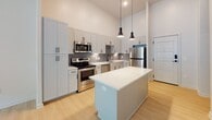 Located at 5001 Libbie Mill East Blvd in Richmond, Virginia, this single-floor residence offers a clean, contemporary design throughout. The kitchen serves as a centerpiece of the home, boasting crisp white shaker cabinetry extending to impressive heights, a grey subway tile backsplash, quartz countertops, and a full suite of stainless steel appliances including a range, microwave, dishwasher, and refrigerator. A central island provides additional prep space and casual seating, while pendant lighting adds a stylish finishing touch beneath the soaring ceilings.

Light hardwood-style flooring flows throughout the main living areas and bedrooms, complementing the neutral palette of soft whites and warm greys. The living area benefits from tall, multi-pane windows that invite abundant natural light and offer views of the surrounding greenery. The elevated window placement enhances the sense of volume and openness.

The hallway leads to well-proportioned bedrooms, one of which includes a generous walk-in closet outfitted with wire shelving on both sides, connecting directly to a private en-suite bathroom. The bathrooms feature neutral tile flooring, white vanities with quartz countertops, and a combination tub and shower. Additional storage is provided by a sliding-door closet accessible from the hallway. The overall ambiance is bright, modern, and move-in ready.