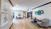 Located at 12201 Avoca Rd in Louisville, KY, this single-floor community amenity space is thoughtfully designed to serve as a hub for socializing, relaxation, and recreation. The welcoming lobby sets an inviting tone with wide-plank light hardwood flooring, dark crown molding accents, and curated teal sculptural wall art. A console table and comfortable seating area create a polished first impression.

The expansive lounge area features a striking herringbone-pattern hardwood floor, plush blue sofas, and an arrangement of accent chairs gathered around coffee tables — ideal for casual gatherings. A wall-mounted TV and abundant natural light from large windows enhance the comfortable atmosphere.

The kitchen and bar area is outfitted with light wood cabinetry, stainless steel appliances, bold blue accent walls, and a generous island with bar stool seating, illuminated by elegant pendant lights. Framed botanical artwork adds a refined touch.

A dedicated fitness center provides cardio equipment including treadmills and ellipticals, with a wall-mounted TV and a window overlooking the surrounding community.

Private lounge nooks feature sectional sofas, geometric patterned rugs, and framed artwork, offering quieter spaces for reading or conversation. Throughout the space, a cohesive palette of teal, blue, and neutral tones creates a modern yet comfortable environment.