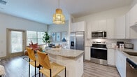 Located at 18210 Park Row Dr in Houston, TX, this single-story, one-bedroom, one-bathroom residence offers a thoughtfully designed open-concept layout. Light wood-style flooring flows throughout the main living areas, complementing the bright, neutral color palette and elevated ceilings that enhance the sense of space.

The kitchen is a standout feature, equipped with stainless steel appliances including a French door refrigerator, electric range, over-the-range microwave, and dishwasher. Crisp white cabinetry extends to the ceiling for ample storage, while granite countertops and a tile backsplash add a polished finish. A peninsula with bar seating connects the kitchen to the dining area, which offers its own distinct space near the entry.

The living room receives generous natural light through large windows with outdoor views, creating an open and airy atmosphere. The primary bedroom is a comfortable retreat with carpeted flooring, a window overlooking greenery, and access to a spacious walk-in closet with built-in shelving and dual hanging rods.

The bathroom features a wide granite-topped vanity with dual sinks, ample cabinetry with gold hardware, and wood-style flooring. A dedicated in-unit laundry room houses a full-size side-by-side washer and dryer, adding everyday convenience to this well-rounded residence.
