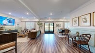 Located in Douglasville, GA, this thoughtfully designed single-floor space combines comfort and style across an open, functional layout encompassing a living room, dining room, and kitchen. The interior is unified by warm wood-look flooring and a consistent color palette of soft whites and sage green wainscoting, lending a cohesive and inviting atmosphere throughout.

The living room offers a comfortable seating arrangement with leather accent chairs, a wood coffee table, and a wall-mounted flat-screen TV above a sleek dark wood credenza. Recessed lighting and a bright window dressed with grid-pattern drapes allow natural light to fill the space.

The dining area is an elegant focal point, anchored by a large dark wood table surrounded by upholstered chairs atop a patterned area rug. Sage green wainscoting lines the walls alongside framed artwork, and a tall fiddle-leaf fig plant adds a natural, organic touch. Windows with coordinating drapes enhance the room's airy quality.

The kitchen is outfitted with dark cabinetry, a green tile backsplash, stainless steel appliances including a French door refrigerator, and a striking gray marble-topped peninsula with bar seating — ideal for casual interaction. Framed artwork above clean white walls completes this polished, functional space.