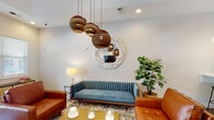 Located at 206 Cedar Branch Ln in Wilmington, NC, this single-story leasing office combines modern design with warm, inviting interiors. The entrance greets visitors with a grand tray ceiling, polished concrete floors, and a bright, open corridor adorned with curated artwork and lush greenery, setting a welcoming tone throughout.

The reception area features dedicated workstations with dark wood desks, glass-partitioned private offices, and display boards showcasing floor plans — all bathed in natural light. A well-appointed lounge area serves as the heart of the space, anchored by a teal channeled sofa, cognac leather armchairs, a gold coffee table, and a striking cluster of sculptural pendant lights overhead. A round woven-frame mirror adds a coastal accent to the textured accent wall.

The kitchenette is outfitted with teal cabinetry, white subway tile backsplash, open wood shelving, a dual sink with matte black fixtures, and a built-in coffee station. An adjoining casual dining area offers mixed seating options alongside a wall-mounted television, ideal for resident gatherings or informal meetings.

A private workstation nook provides a built-in desk, sleek wall sconce, and a comfortable chair — a quiet retreat for focused tasks. Together, these spaces create a cohesive, functional, and design-forward environment.