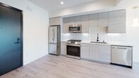 This single-floor space showcases a clean, contemporary design throughout. The open-concept layout is unified by light wood-toned flooring that extends seamlessly across the living areas and bedrooms, creating a bright and cohesive aesthetic.

The kitchen is well-appointed with floor-to-ceiling light wood cabinetry, stainless steel appliances including a gas range, microwave, refrigerator, and dishwasher, complemented by a geometric white tile backsplash and light stone countertops. Recessed lighting and under-cabinet fixtures ensure the space is well-lit.

The living area benefits from large sliding glass doors that open to a private balcony, offering views of surrounding greenery and filling the room with natural light. Recessed ceiling lights add to the bright, airy ambiance.

The bedrooms feature crisp white walls, recessed lighting, and ceiling fans. One bedroom includes a built-in closet with frosted sliding glass doors, adding a refined touch. Additional rooms offer ample wall space and multiple entry points.

The bathroom presents a polished finish with large-format marble-style porcelain floor tiles, a floating wood-toned vanity, an illuminated mirror, and a clean white shower area, all tied together with modern chrome fixtures.