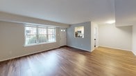 This single-floor residence offers a thoughtfully designed layout that balances comfort and functionality. The open living area is a welcoming centerpiece, featuring rich hardwood-style flooring and large multi-pane windows that invite an abundance of natural light and provide views of the surrounding greenery. A front entry door with a sidelight panel adds to the bright, airy atmosphere of the space.

The kitchen is efficiently arranged in a galley-style configuration, showcasing white shaker cabinetry, light stone-look countertops, a classic subway tile backsplash, and a full suite of appliances including a gas range, stainless steel microwave, dishwasher, and refrigerator. A window above the sink further enhances the kitchen's natural light. The kitchen opens to the main living area through a convenient pass-through cutout.

A hallway connects the living spaces to the private areas of the home, which include a spacious bedroom finished with plush carpeting, large windows, and ample closet space. The full bathroom is clean and functional, featuring a tiled tub-and-shower combination with brushed nickel fixtures, a toilet, and a vanity with storage. Neutral gray walls, white trim, and consistent hardwood-style flooring throughout the main areas create a cohesive, modern aesthetic across the entire residence.