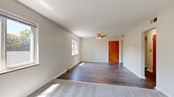 This single-floor unit offers a practical and well-organized layout across two bedrooms, one bathroom, a kitchen, and a hallway. The living area features a combination of dark hardwood flooring and plush carpet, creating a clear distinction between zones. Multiple windows allow natural light to fill the space, while a ceiling fan with a light fixture adds both function and a finishing touch to the main living area. The warm-toned wooden entry door adds a classic detail to the otherwise neutral, white-walled interior.

The generously sized primary bedroom is carpeted and benefits from a large window overlooking lush greenery, providing a serene outdoor view. The second bedroom is similarly carpeted with neutral walls and access to natural light. Both rooms offer clean, straightforward layouts suited for flexible furniture arrangements.

The kitchen is notably updated, featuring stainless steel appliances including a full-size refrigerator, range, and microwave, complemented by white cabinetry, light stone-style countertops, subway tile backsplash, and hardwood-style flooring. A window above the counter provides additional natural light.

The bathroom is tiled in classic white, complete with a sliding glass shower enclosure over a tub, a vanity with mirror, and a small window for ventilation. The overall ambiance of the unit is clean, bright, and move-in ready.