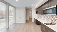 Located at 1420 E Howell St in Seattle's Capitol Hill neighborhood, this efficiently designed studio unit offers a thoughtful layout across a single floor. The open-plan kitchen and living area serves as the heart of the space, showcasing rich dark-toned cabinetry with sleek hardware, white quartz countertops, stainless steel appliances including a built-in microwave and refrigerator, and a striking mosaic tile backsplash with multicolor accents. Light wood-look flooring runs throughout, lending warmth and continuity to the interior. A standout feature of the living area is the expansive floor-to-ceiling windows that wrap around the corner, flooding the space with natural light and offering open views of the surrounding streetscape and greenery. The entrance leads naturally into the main living area, with a dedicated closet providing practical storage. The bathroom is finished with large-format tile flooring, a soaking tub with a tiled shower surround, and a vanity with mirror — offering a clean, functional design. Recessed lighting throughout ensures a bright and well-lit atmosphere. The unit's contemporary finishes and efficient use of space make it a well-appointed residence in Seattle's vibrant East Capitol Hill area.