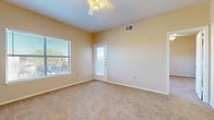 This single-story space is designed with a straightforward, functional layout visible across its several rooms. The living area is generously sized, finished with neutral beige carpet and painted in a warm cream tone that carries throughout the unit. A ceiling fan with integrated light fixture overhead provides both airflow and ambient lighting, while a large window and an exterior door with a glass panel allow abundant natural light and outdoor views. The open feel of this room is reinforced by clean, white baseboards and well-maintained walls.

The kitchen follows a galley-style configuration, featuring light wood cabinetry on both sides, light-toned laminate countertops, and wood-look plank flooring. White appliances — including a range, dishwasher, and refrigerator — are included. An electrical panel is accessible within the kitchen area.

The bedrooms mirror the living area's aesthetic, each carpeted, naturally lit by windows with outdoor views, and fitted with ceiling fans. The rooms offer a clean, neutral palette suited for a range of furnishing styles.

The bathroom is finished with wood-look flooring, a wood-tone vanity with overhead cabinetry, a white countertop, and a full-size bathtub, completing the unit's consistent and practical interior design.